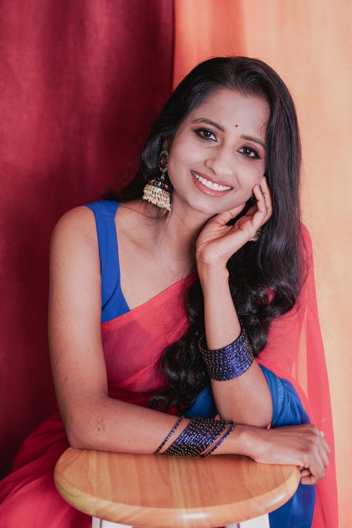 Free A woman in colorful traditional attire smiling while seated indoors, conveying warmth and elegance. Stock Photo
