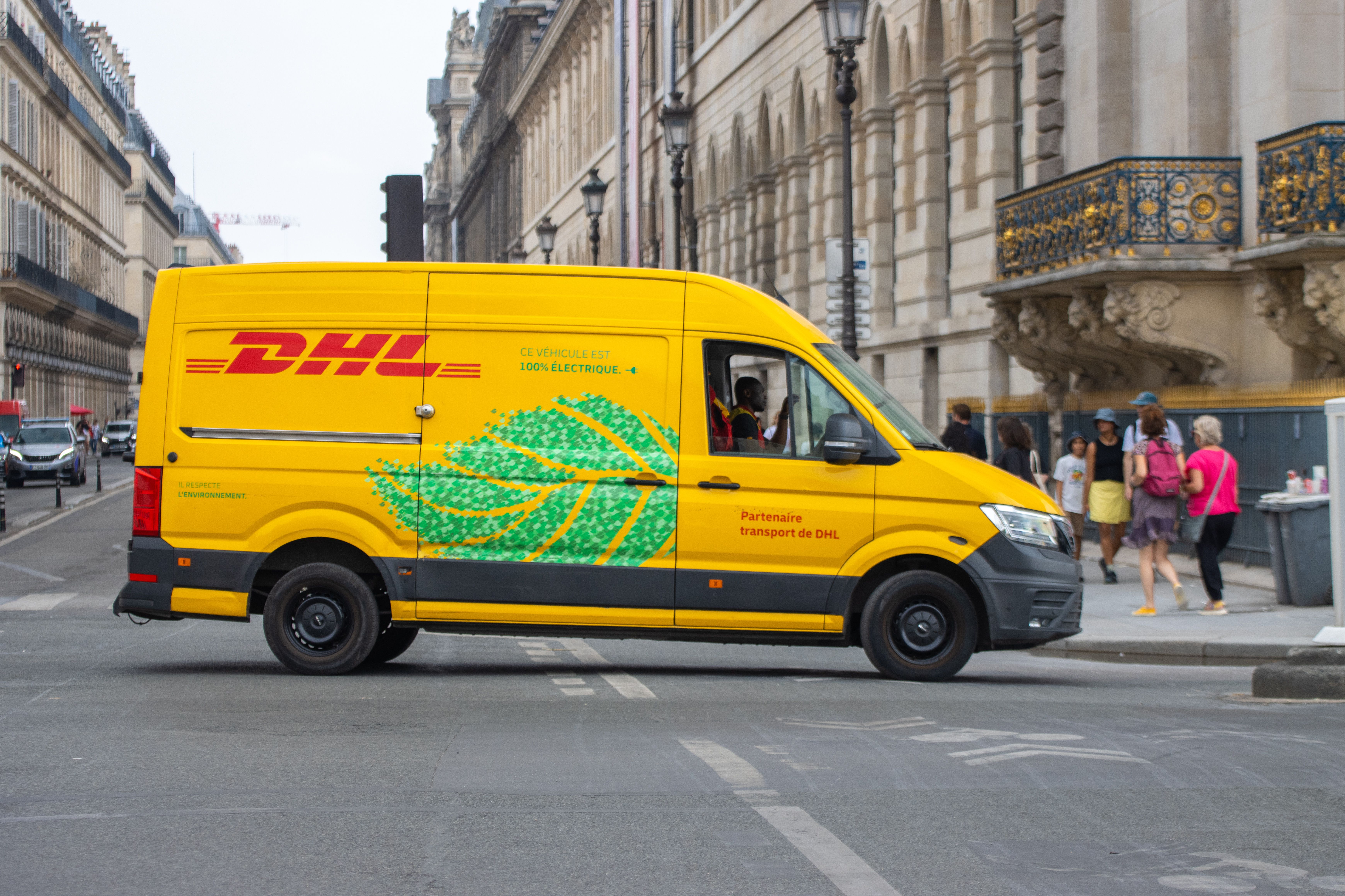 Electric delivery van navigating through a busy Parisian street on a sunny day.