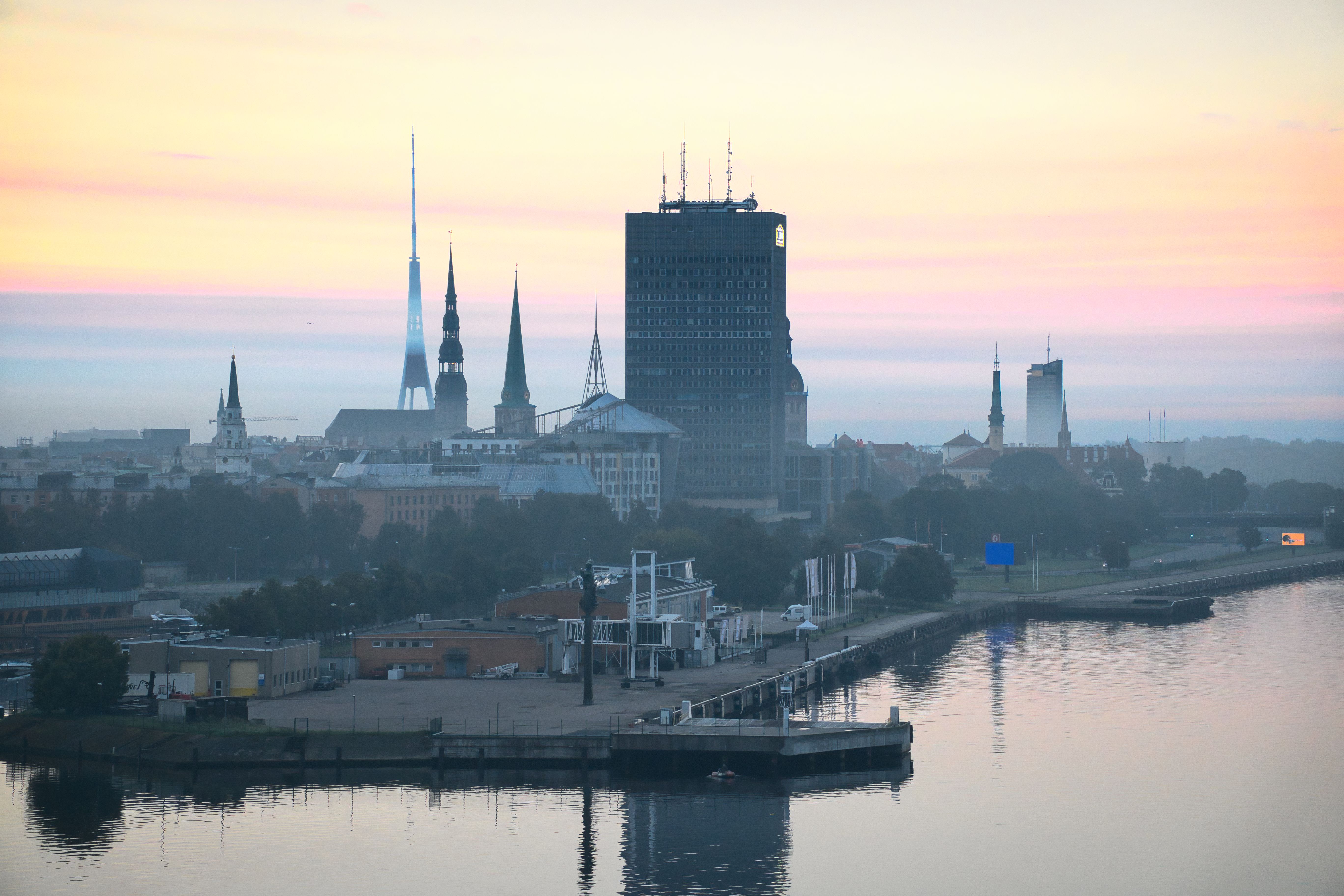 Beautiful sunrise view of Riga cityscape with iconic spires and serene river reflections.
