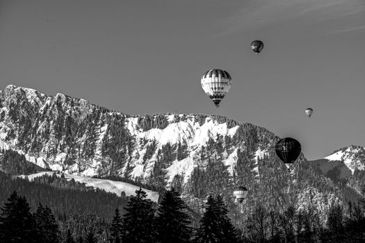 Black and white photo of hot air balloons over the snowy Swiss Alps, capturing a serene winter scene.