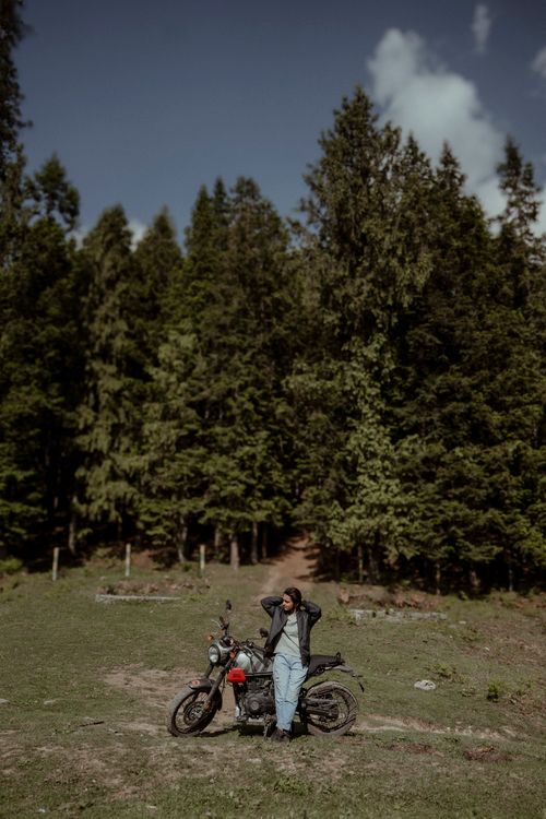 Free Young traveler with motorcycle by trees in Indian forest, capturing adventure and nature. Stock Photo
