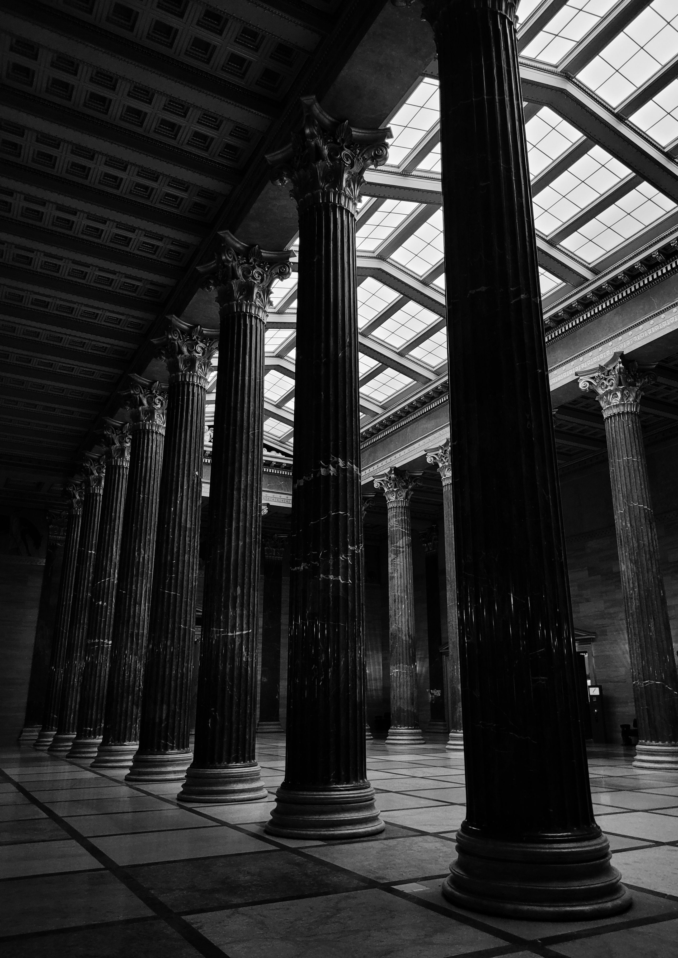 Dramatic black and white photo of a classical hall with tall pillars and intricate ceiling details.