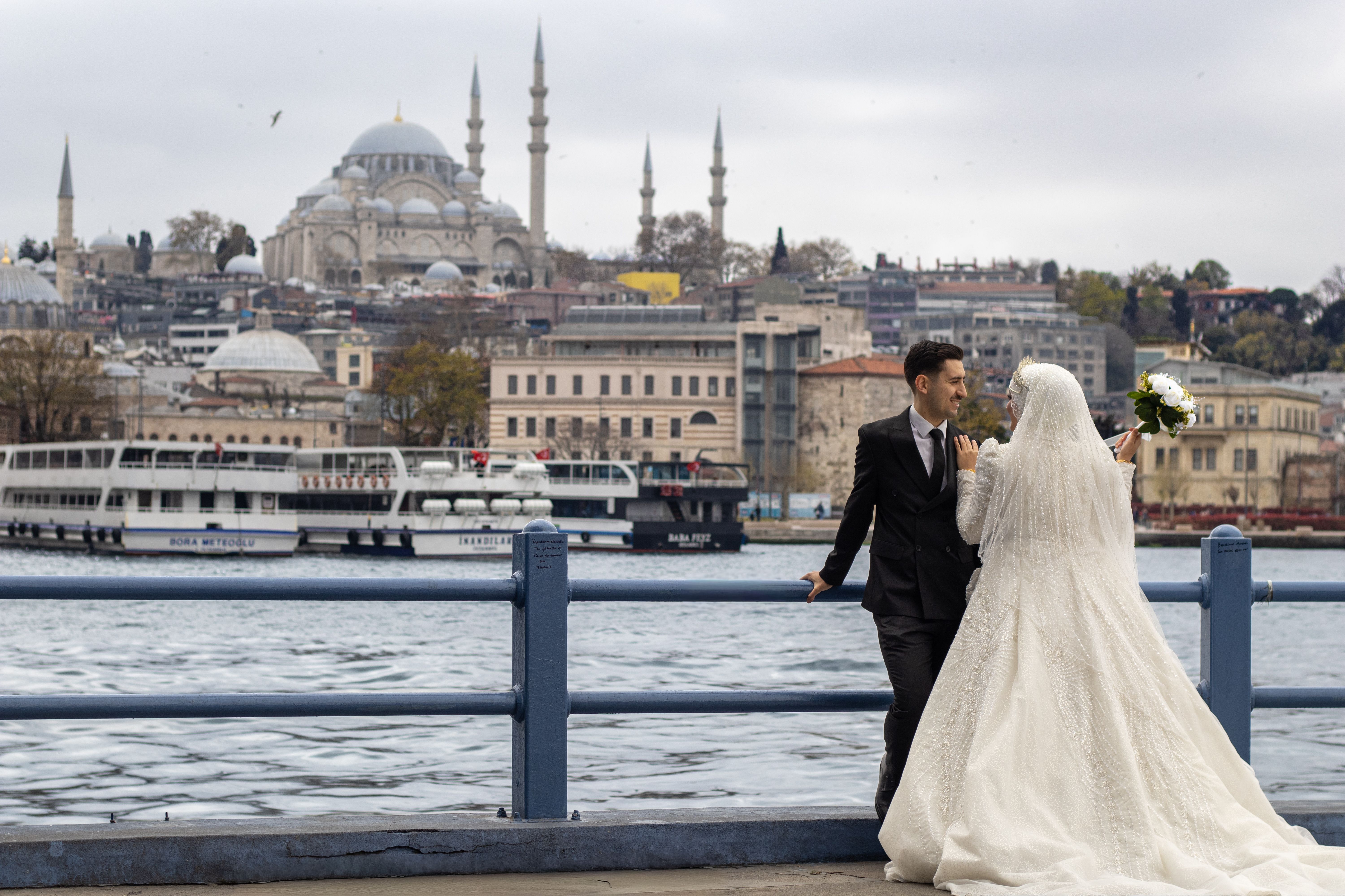 Bride and groom by Bosphorus with Istanbul skyline and Suleymaniye Mosque in background.