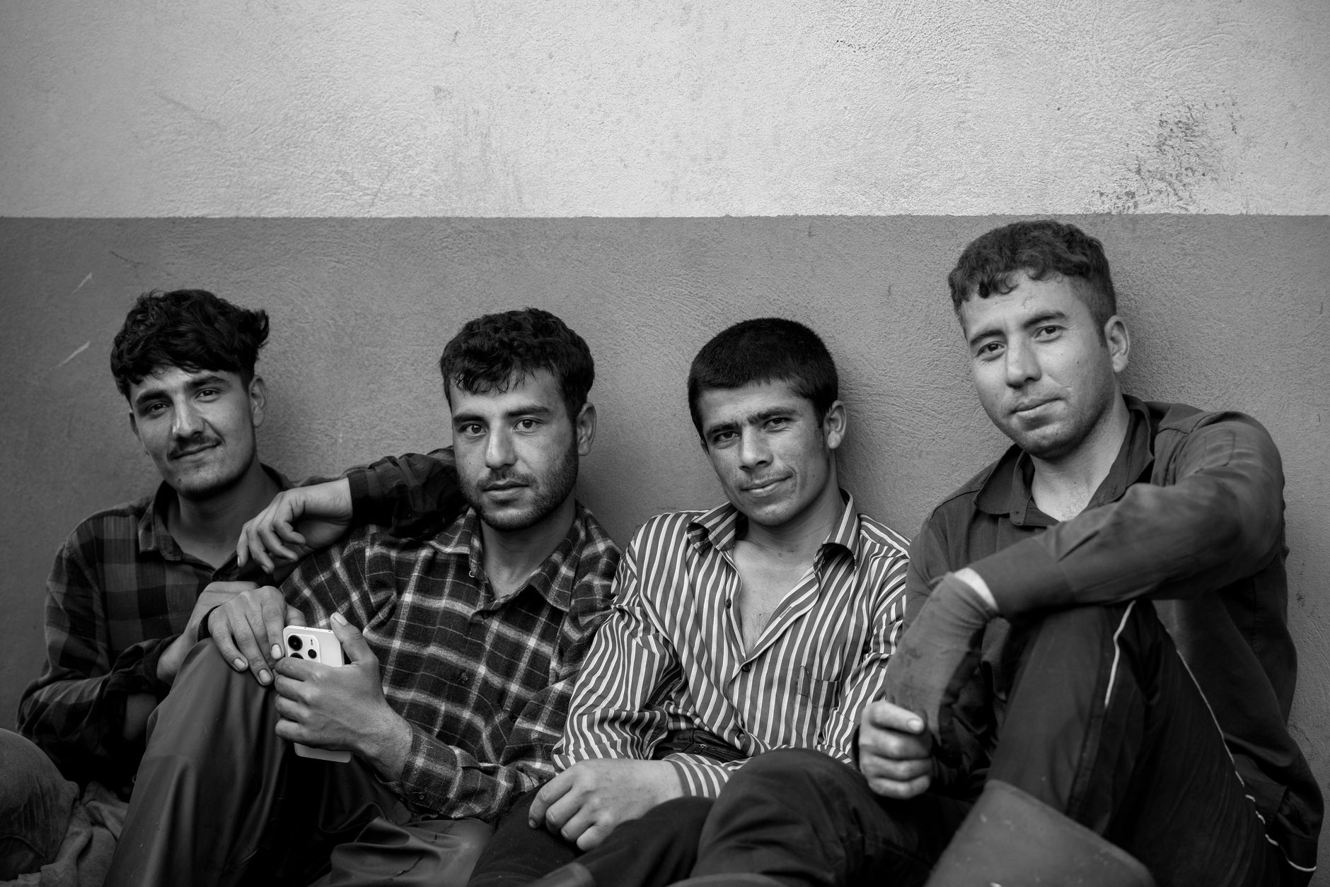 Black and white photo of four young men sitting against a wall, relaxed and smiling. — free online jigsaw puzzle on JigsawPuzzlesFreeOnline.org