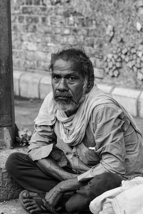 Free Black and white portrait of an elderly man sitting on the street, capturing deep emotion. Stock Photo