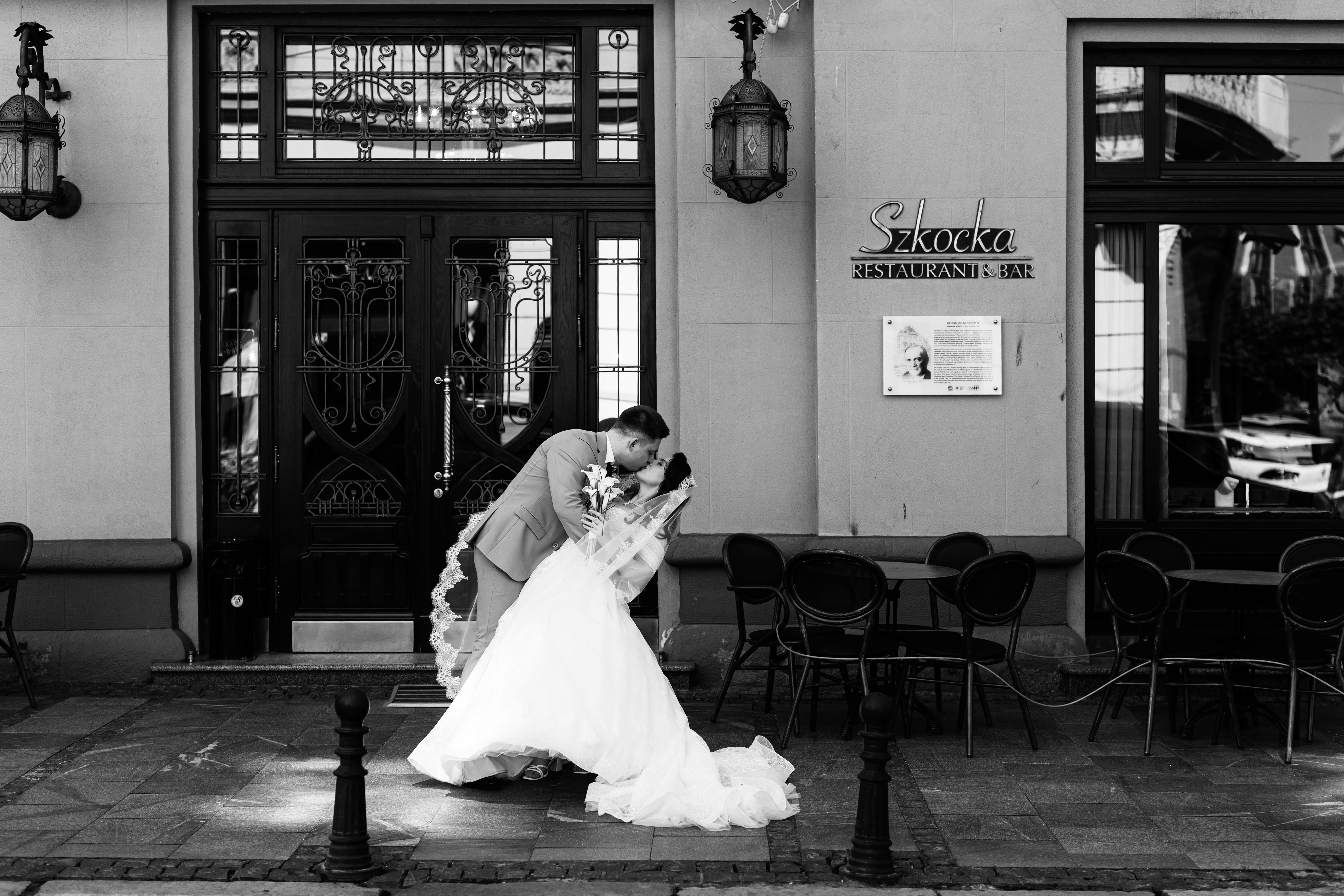 Elegant black and white photo of a couple kissing in front of a restaurant.