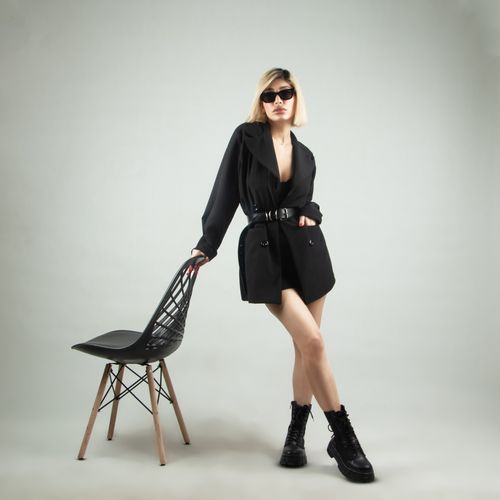 Free Fashionable woman in black attire with sunglasses posing indoors next to a chair. Stock Photo