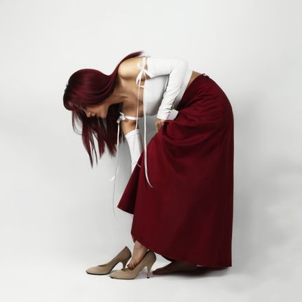 Woman in a white top and long maroon skirt against a pale wall — photo by Reza Roshan on Pexels