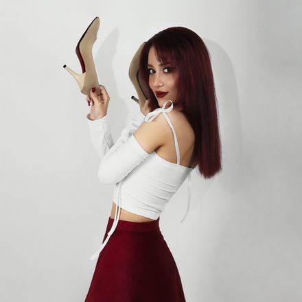 Studio shot of a woman holding a pair of nude heels — photo by Reza Roshan on Pexels