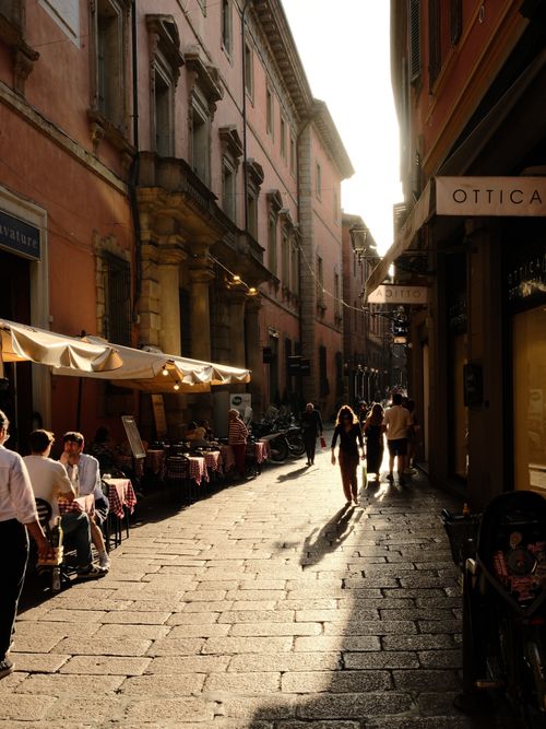 Free A picturesque street in Bologna, Italy, showcasing outdoor cafes and historic architecture during sunset. Stock Photo