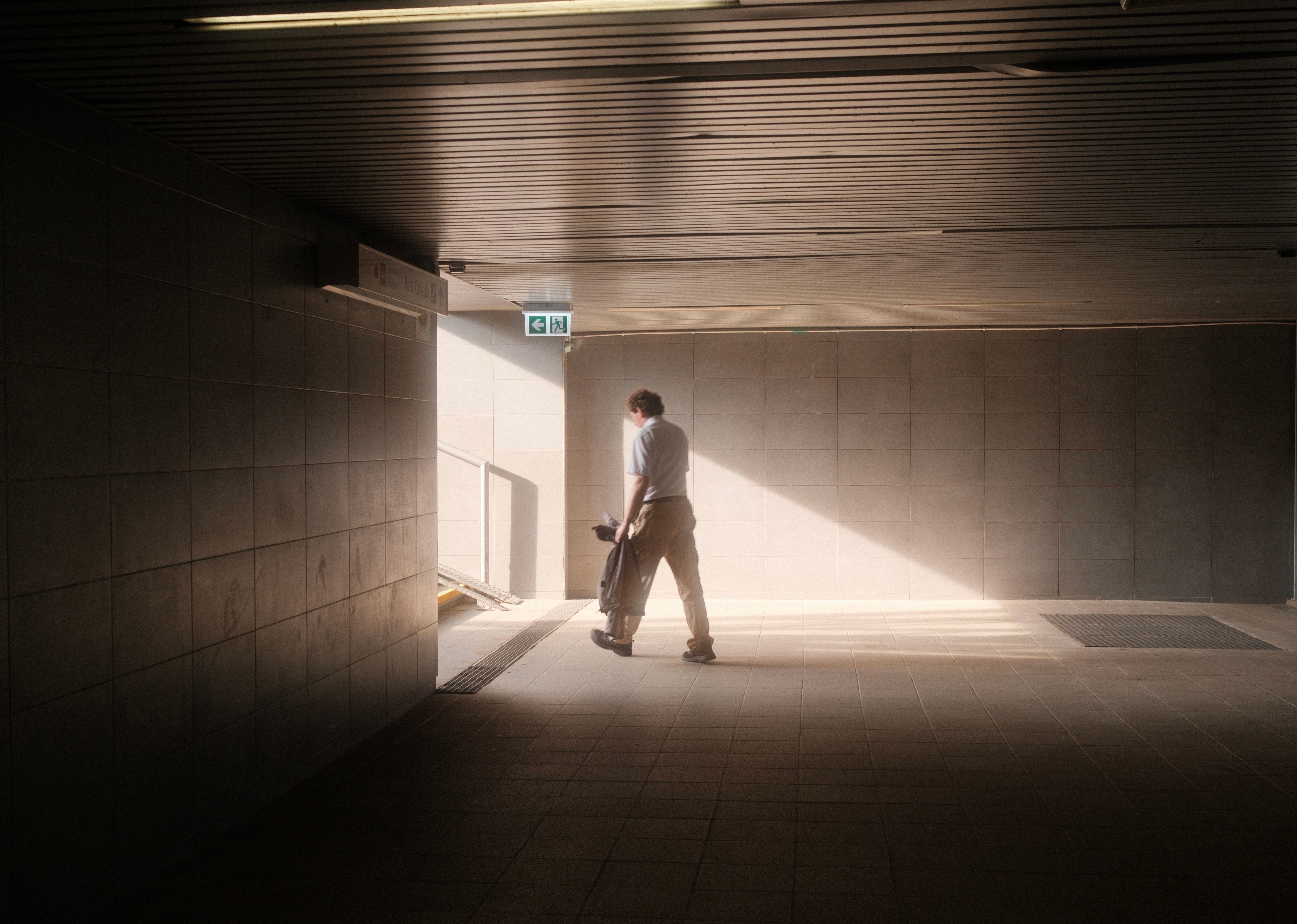 A solitary man walks through a sunlit tunnel in an urban setting, capturing a serene moment.