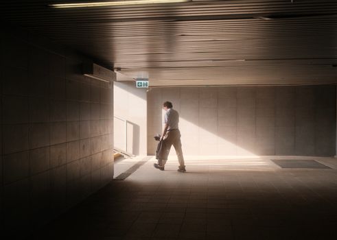 A solitary man walks through a sunlit tunnel in an urban setting, capturing a serene moment.