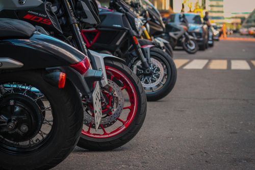 Free Row of parked motorcycles on an urban street, featuring close-up of front wheels and vibrant colors. Stock Photo