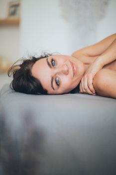 A serene portrait of a woman relaxing on a bed, smiling softly indoors.
