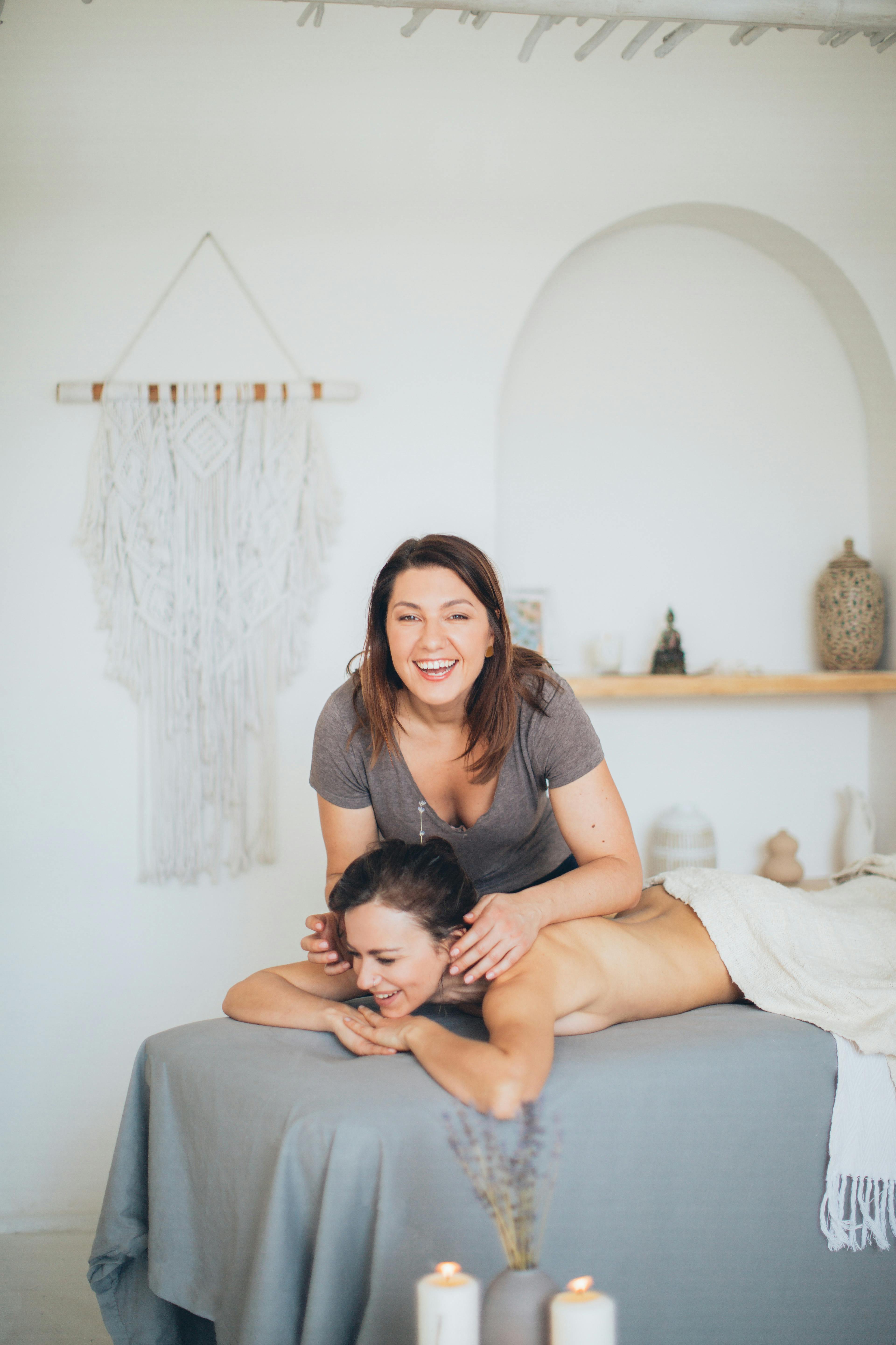 a woman in gray shirt massaging a topless woman lying down