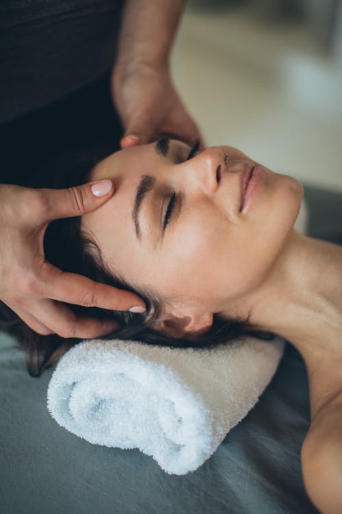 Free A Woman Lying Down while Having Her Head Massage by a Person Stock Photo