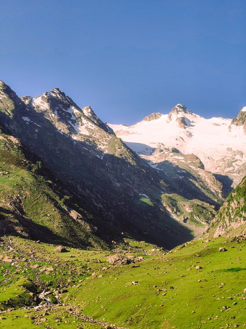 Free Breathtaking view of a lush green valley with towering snowy mountains under a clear blue sky. Stock Photo