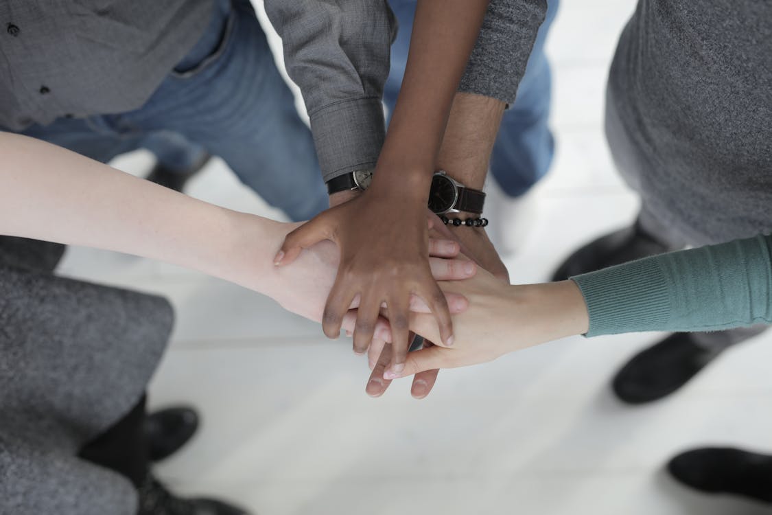 Crop from above of faceless multiracial friends in casual clothes uniting hands after coming to agreement while standing on light grey ceramic floor
