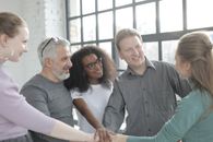 Cheerful diverse colleagues joining hands after coming to agreement
