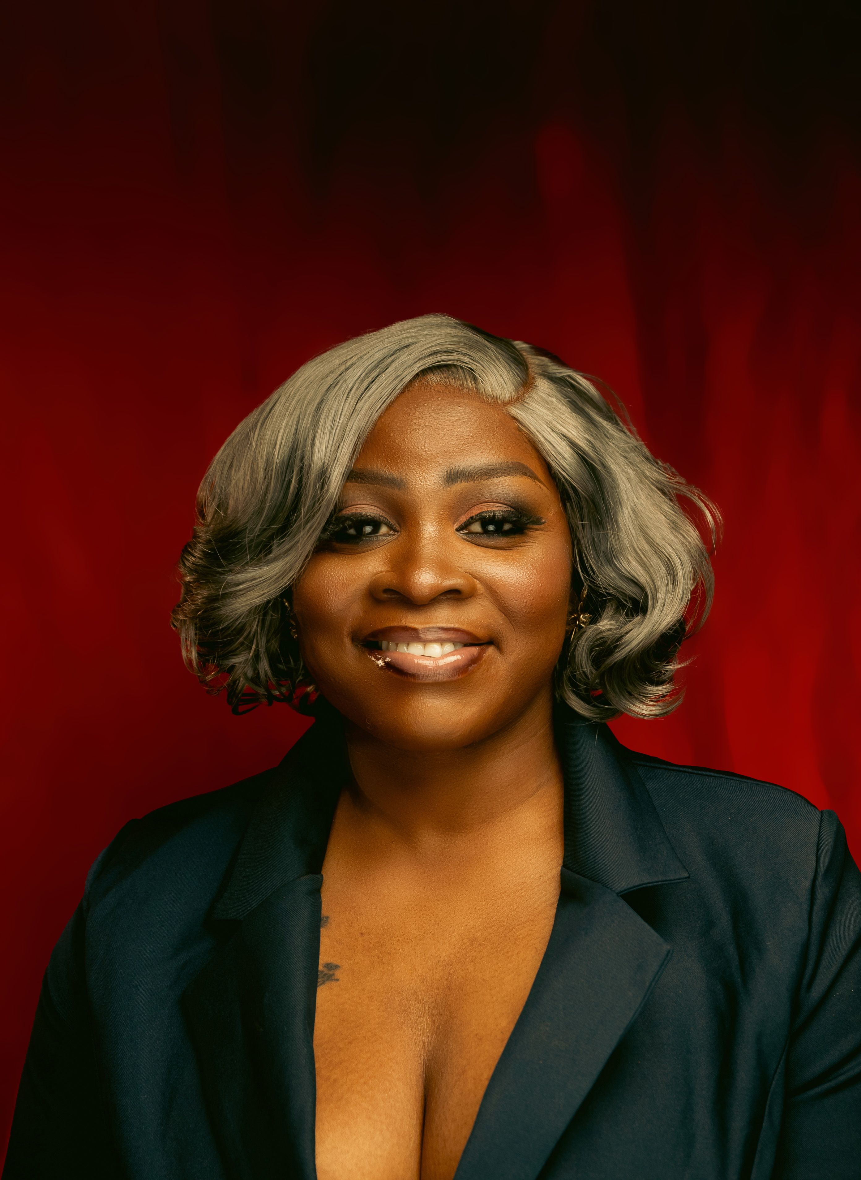 Elegant portrait of a smiling woman in a navy blazer with a red background.