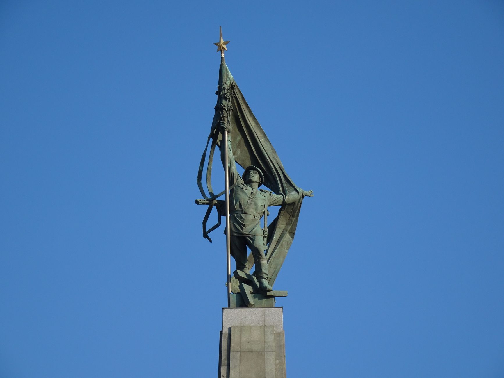 Close-up of a Soviet soldier statue holding a flag in Bratislava against a clear blue sky.