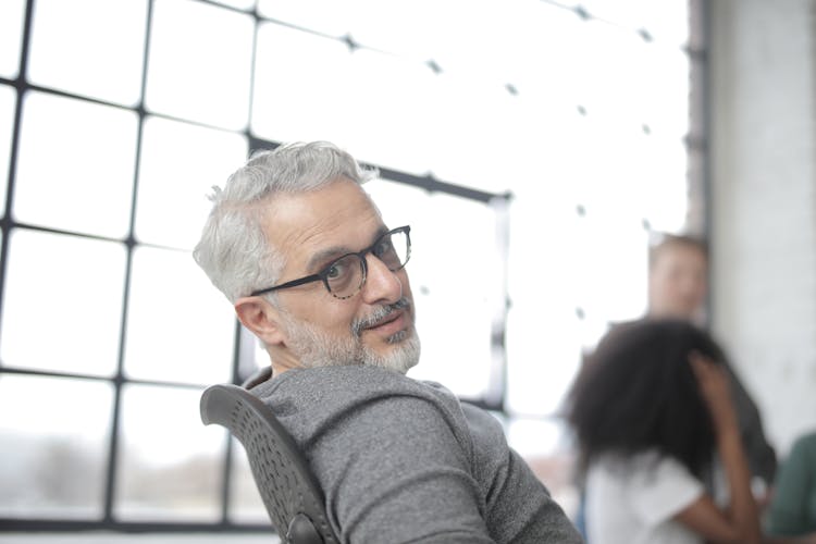 Senior Confident Businessman Sitting In Computer Chair During Job With Colleagues In Daytime