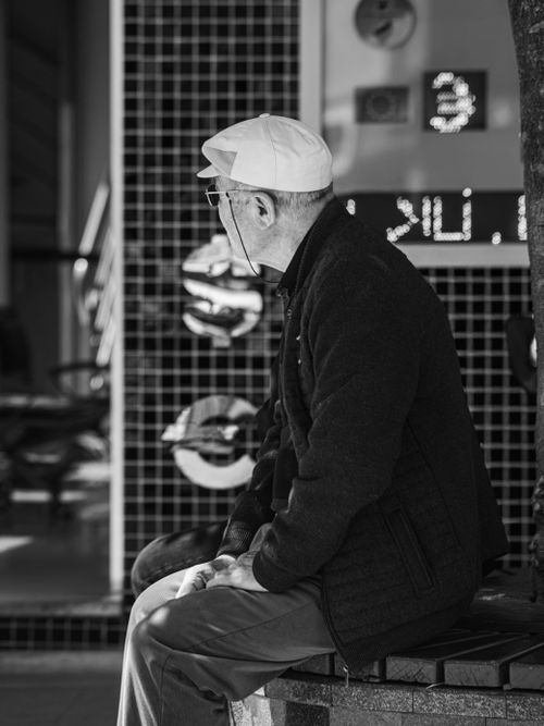 Free Black and white photo of a senior man sitting on a bench in an urban environment. Stock Photo
