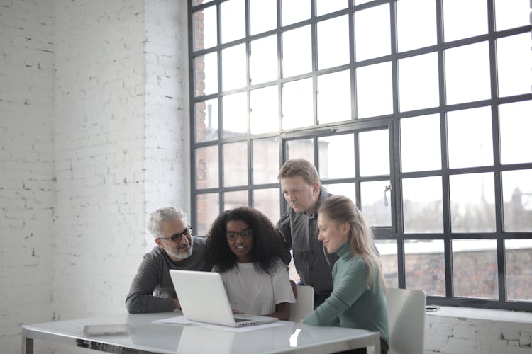 Cheerful Diverse Colleagues Of Different Ages Using Laptop In Creative Workplace