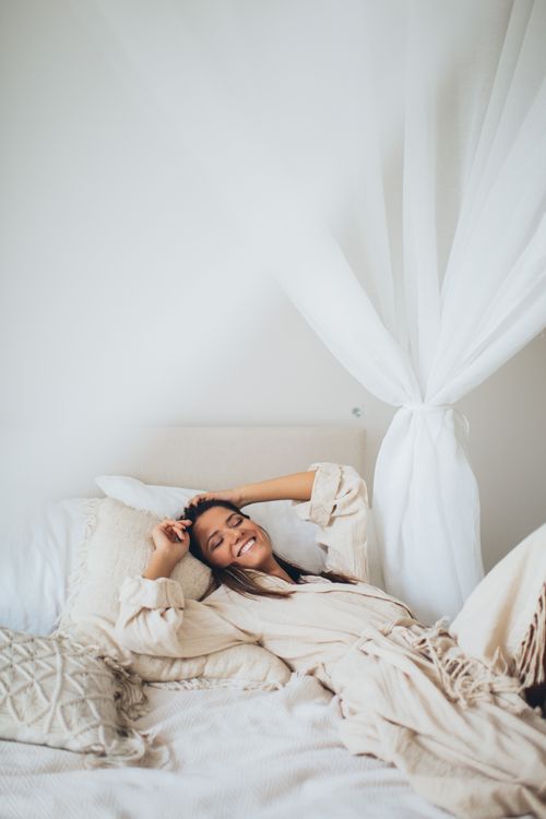 Free Woman smiling and relaxed in bed wearing a bathrobe in a cozy bedroom. Stock Photo