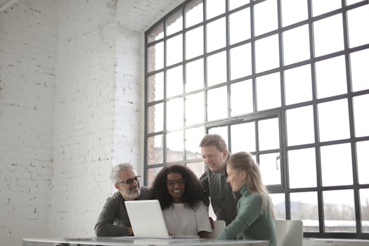 Group of colleagues collaborating around a laptop in a bright, modern office space.
