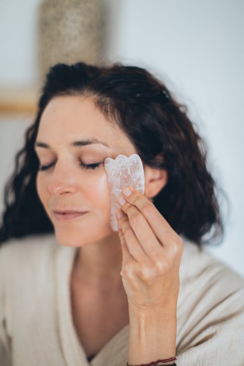 Free A Woman Using a Gua Sha on Her Face Stock Photo
