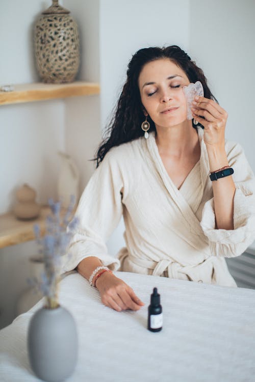 Free A Woman Wearing a Bathrobe while Using a Gua Sha on Her Face Stock Photo