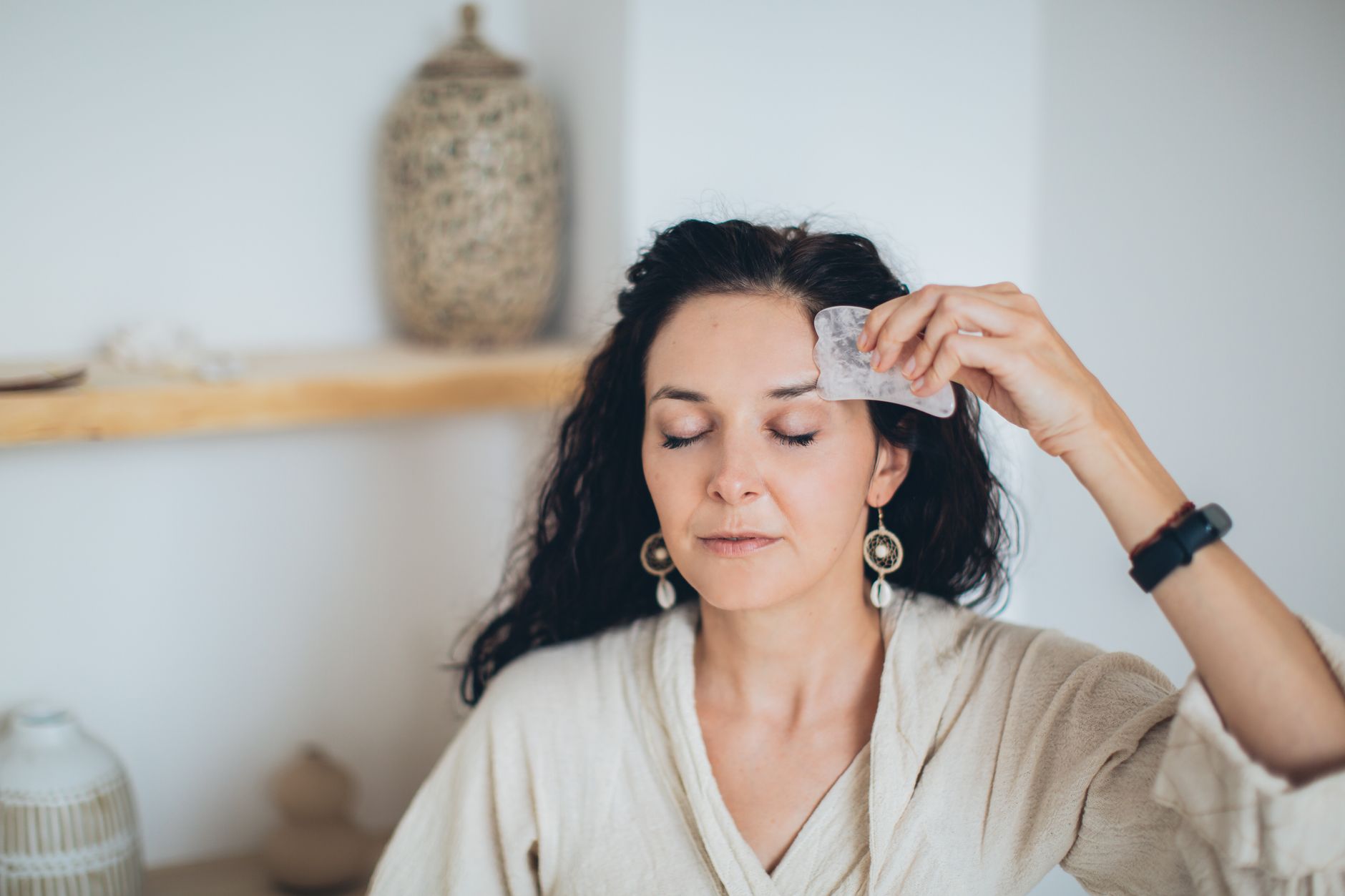 Mains de thérapeute appliquant la technique du gua sha sur le front d’une cliente en institut