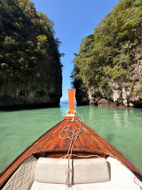 Free A traditional Thai long-tail boat sails through turquoise waters between limestone cliffs under a clear blue sky. Stock Photo