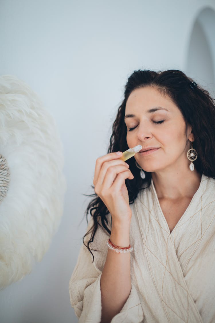 A Woman Holding A Small Bottle While Smelling It