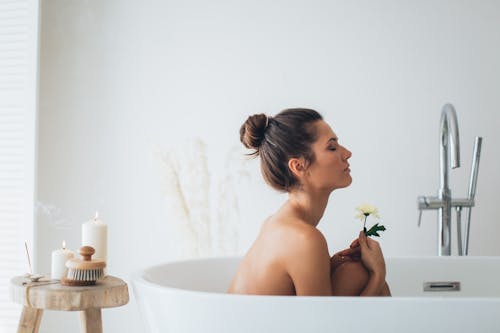 Topless Woman Sitting on White Ceramic Bathtub Holding Flower