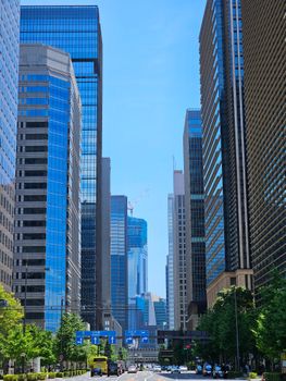 High-rise buildings line a bustling street in Tokyo, Japan, under a clear blue sky.