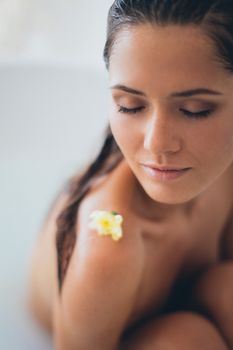 Serene portrait of a woman relaxing with a flower on her shoulder, embodying tranquility.