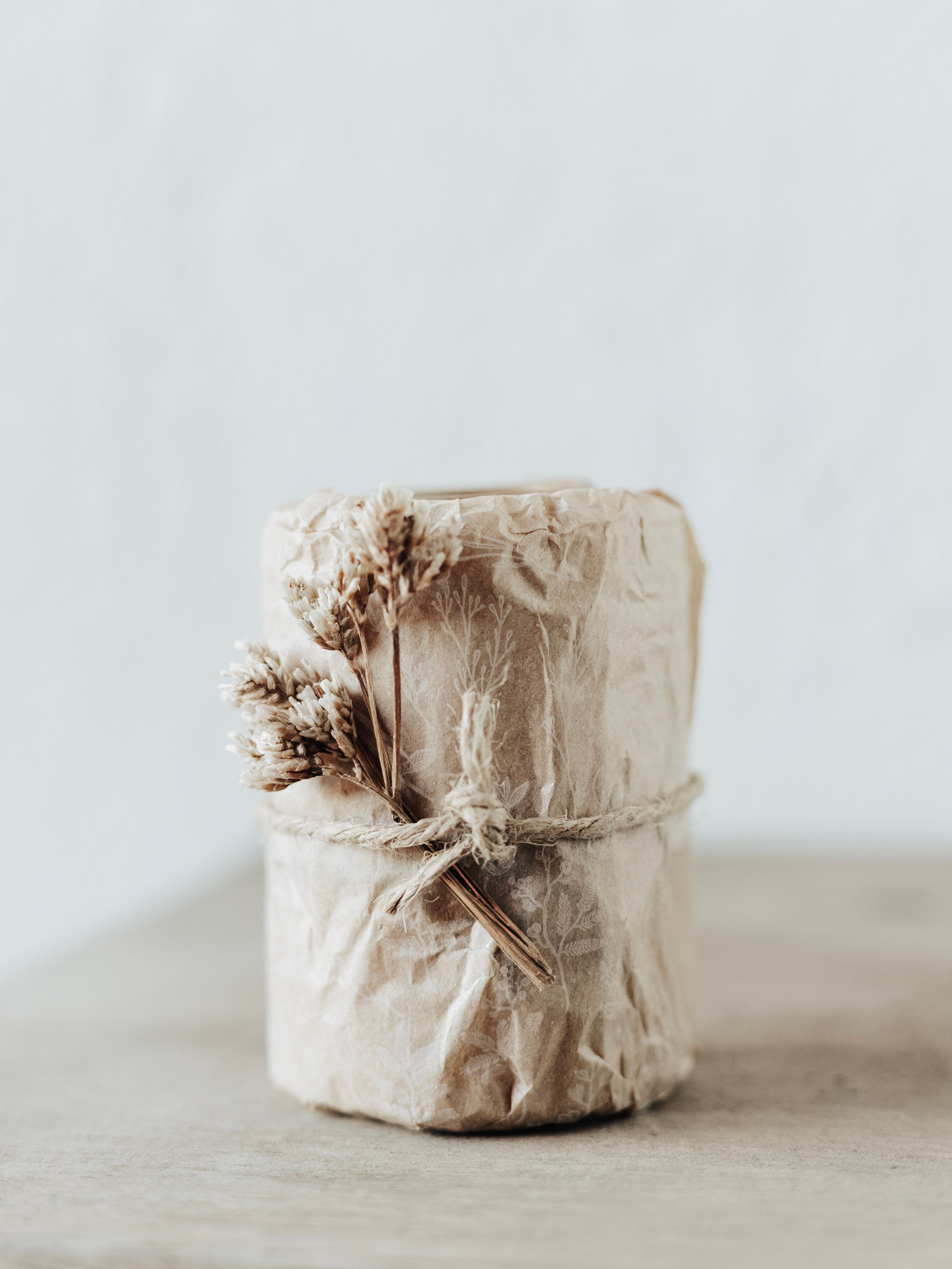 A beautifully wrapped rustic candle with dried floral decoration on a minimalist background.
