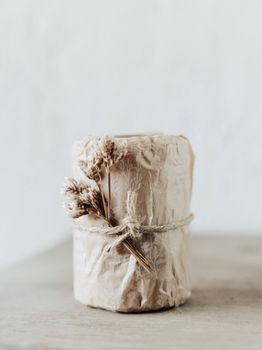 A beautifully wrapped rustic candle with dried floral decoration on a minimalist background.