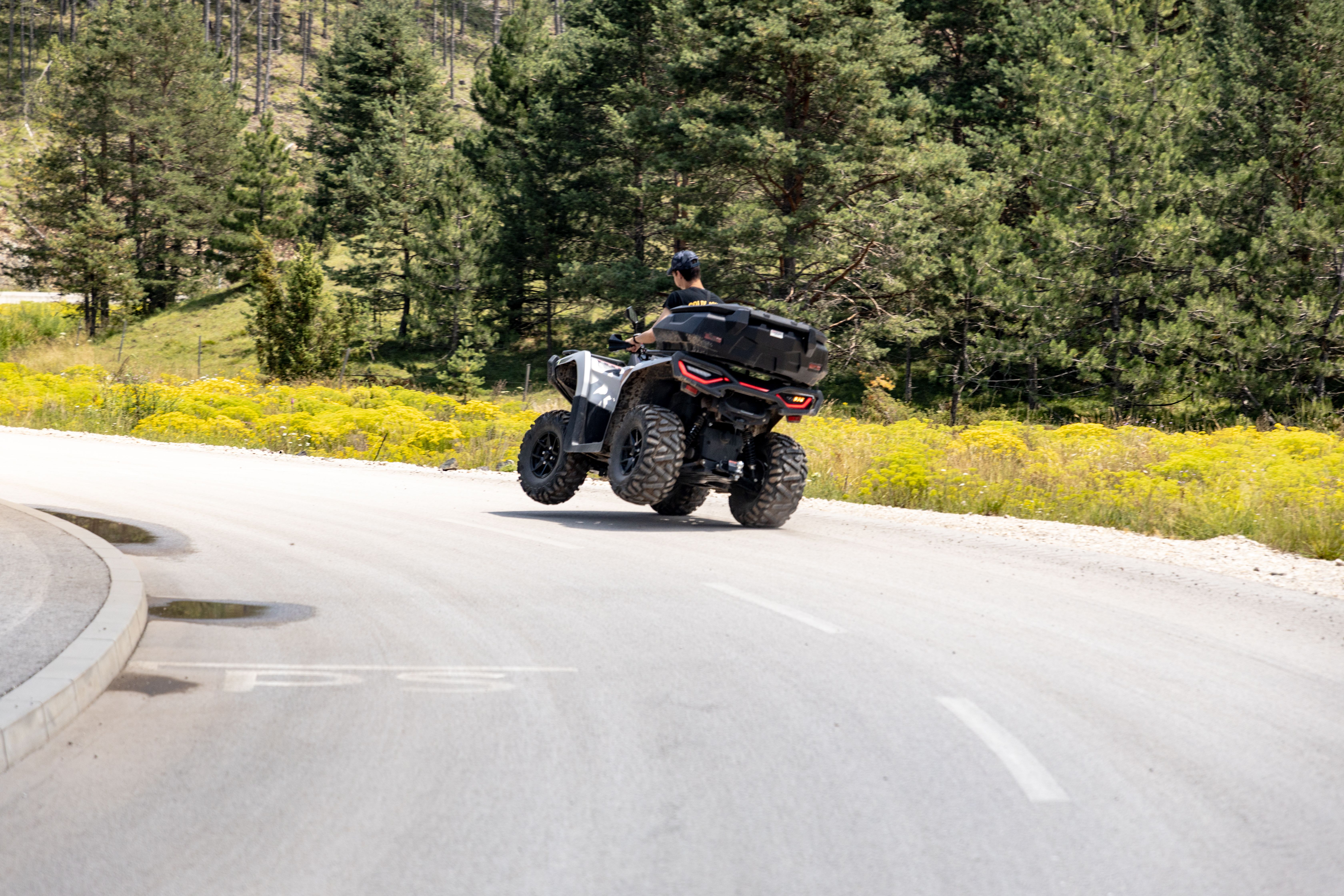 Man rides an ATV on a sunny road through Zlatibor, Serbia, surrounded by lush greenery.