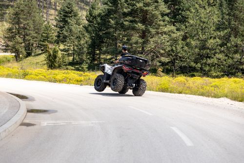 Free Man rides an ATV on a sunny road through Zlatibor, Serbia, surrounded by lush greenery. Stock Photo