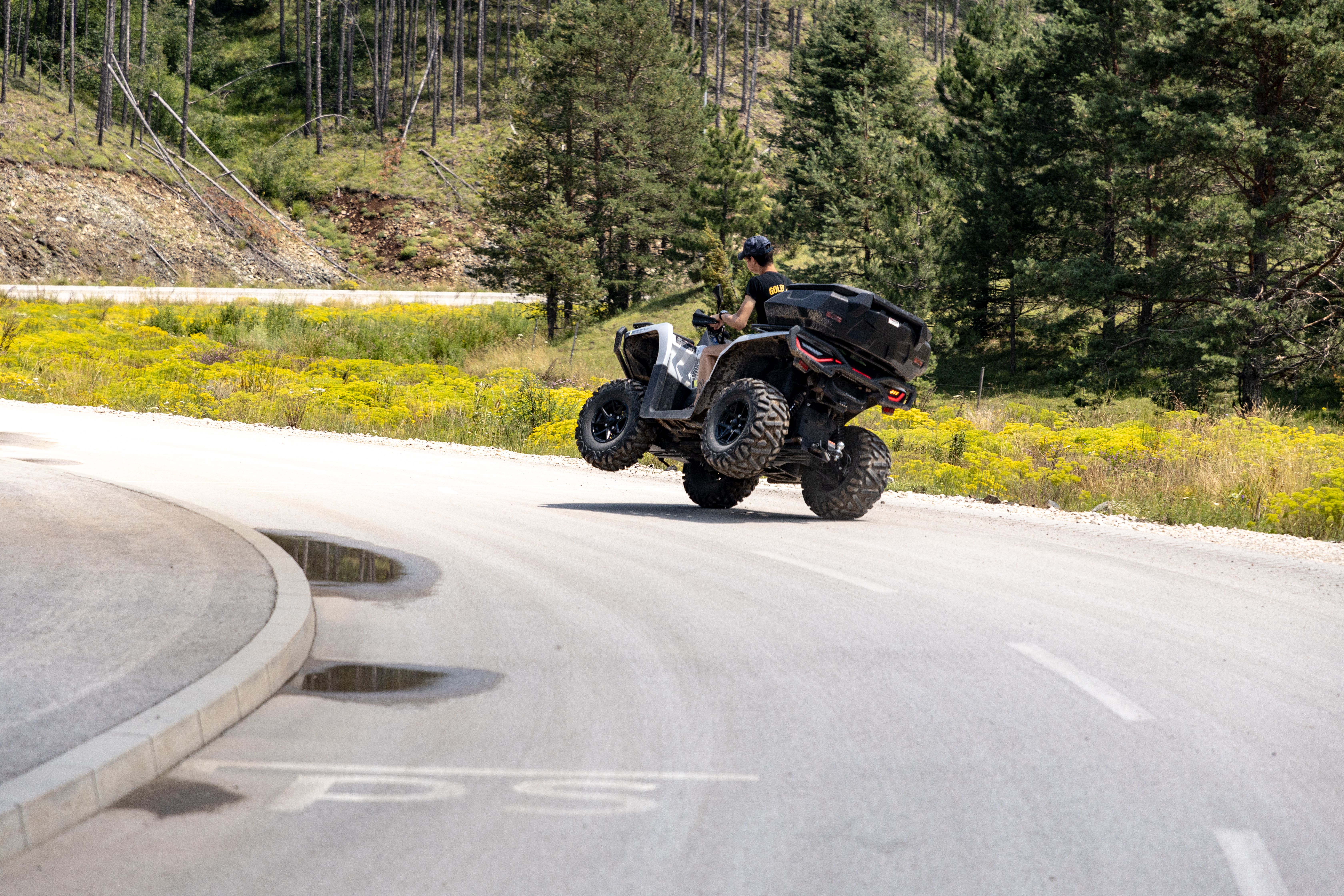 Thrilling ATV maneuver on a scenic mountain road in Zlatibor, Serbia, surrounded by lush greenery and vibrant summer scenery.