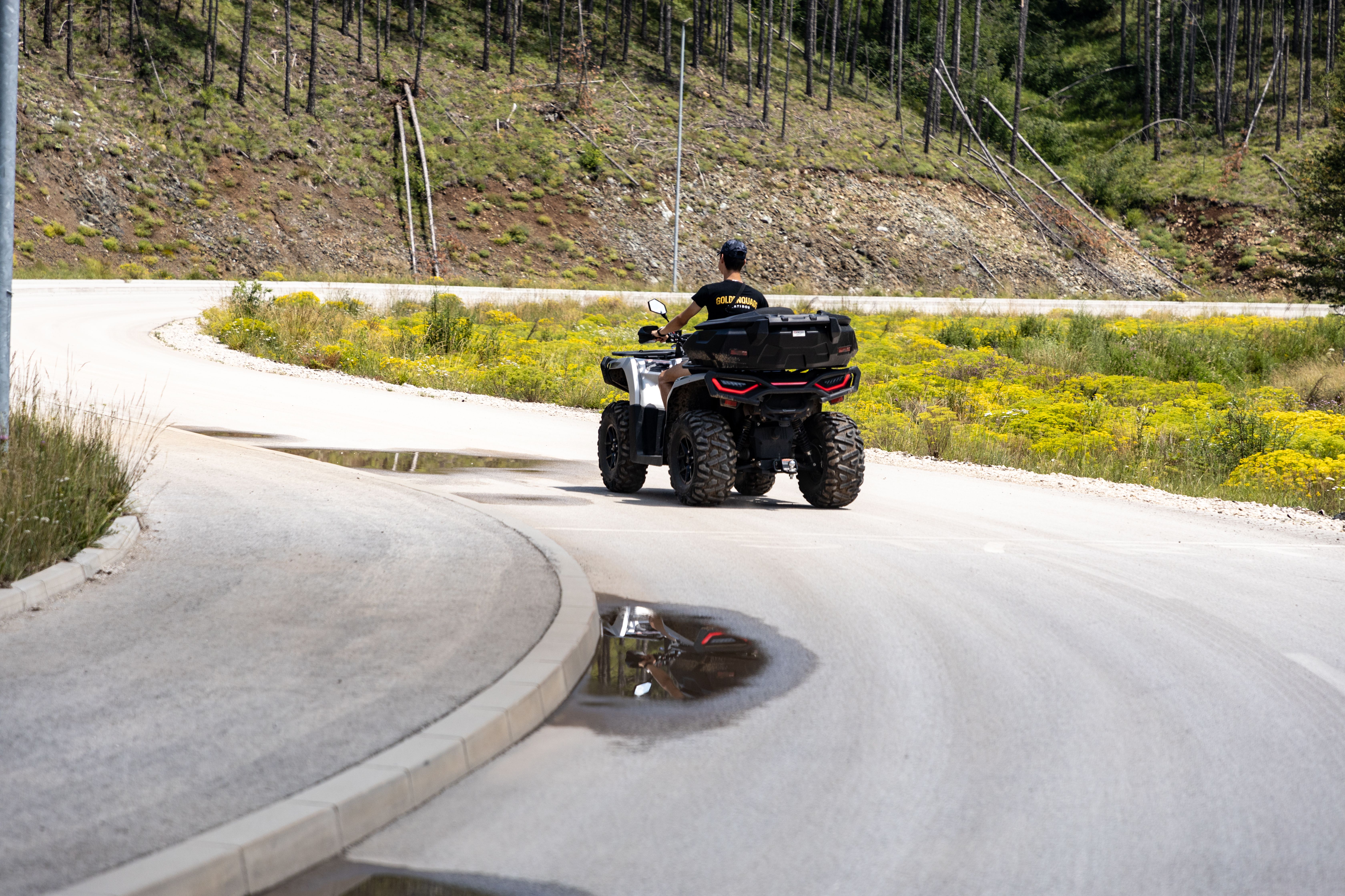 A person riding an ATV on a winding road in Zlatibor, Serbia, surrounded by lush greenery and hills.