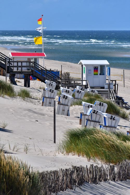Free Scenic beach view with sand dunes, beach chairs, and a lifeguard station under a clear blue sky. Stock Photo