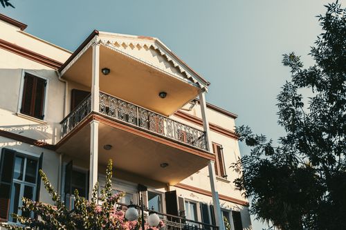 Free Elegant colonial-style home with balcony under a clear blue sky, surrounded by greenery. Stock Photo