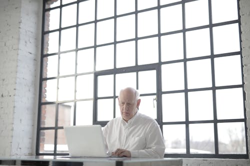 Man in White Shirt Sitting by the Table Using Macbook