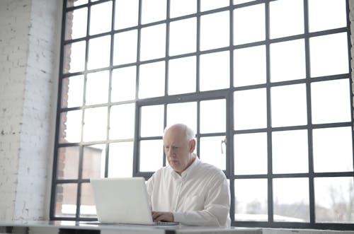Man in White Shirt Sitting in Front of Macbook