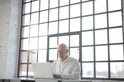Free Focused senior man working on laptop in bright modern office with large windows. Stock Photo