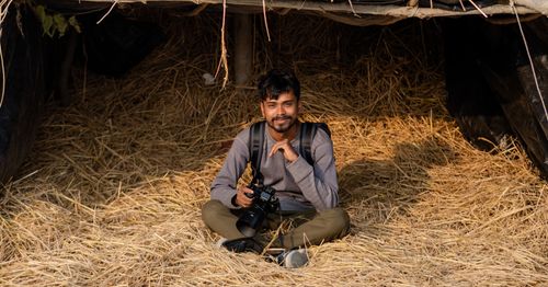 Free Young male photographer relaxing with camera in a straw-filled shelter in Bangladesh. Stock Photo